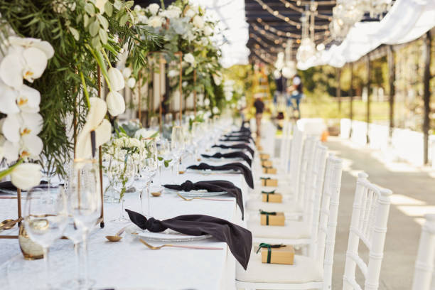 A long table is set for an outdoor event, adorned with white flowers and elegant place settings.
